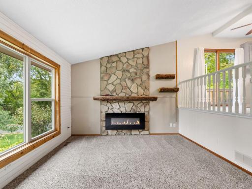 Bright and inviting, this main-level living room features a stunning stone fireplace, vaulted ceiling, plush carpeting, and large windows overlooking the beautiful outdoor setting. An open layout provides a comfortable and space for relaxing!