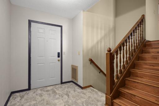 Welcoming entry foyer with durable tile-look flooring and wood staircase.