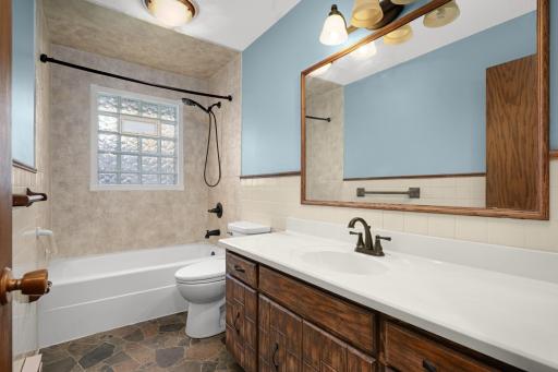 Upper-level full bathroom with tub/shower surround, vanity and glass-block window