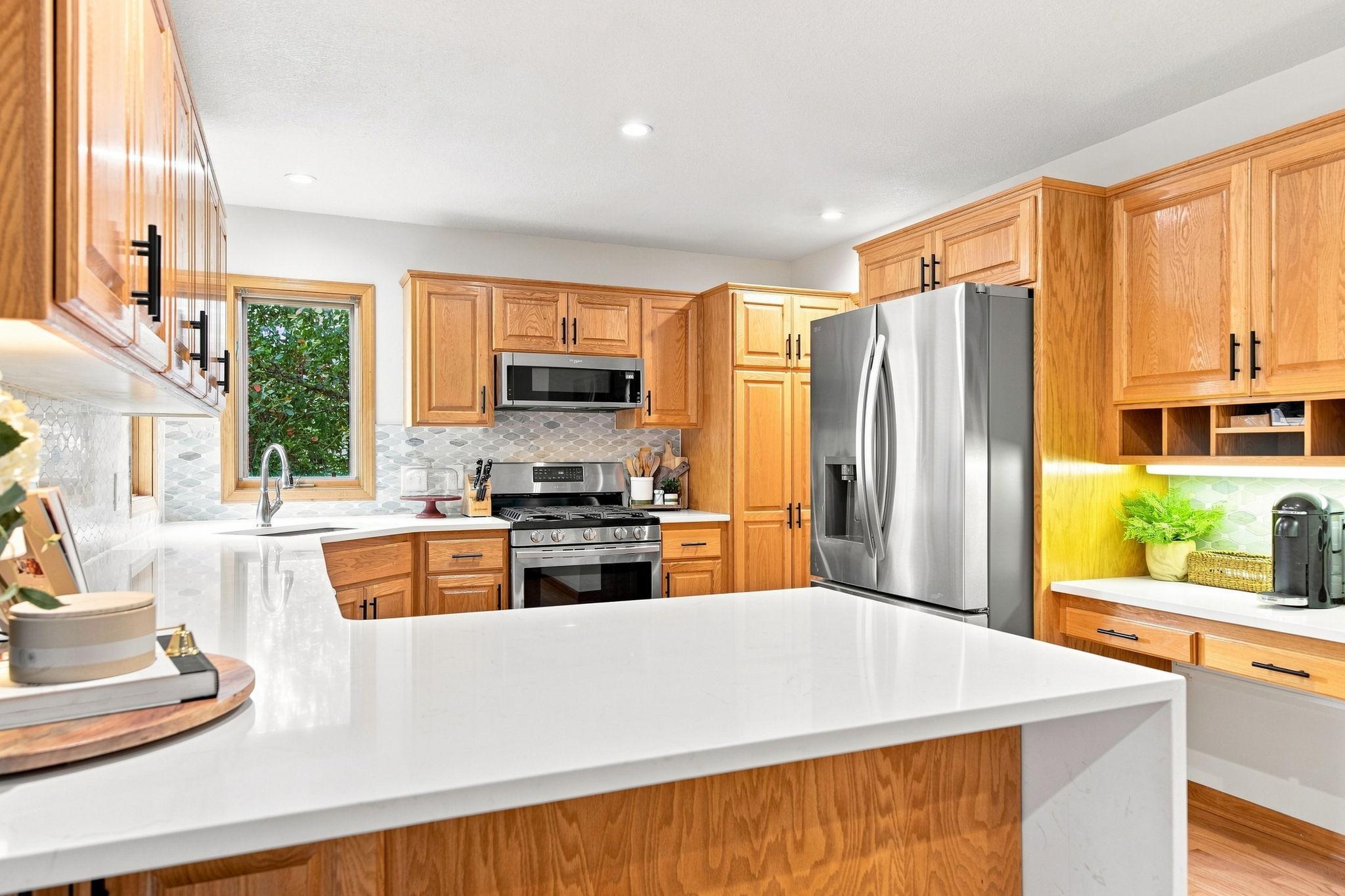 Stunning updated kitchen featuring quartz countertops, tile backsplash, and new refrigerator, gas range, and microwave.