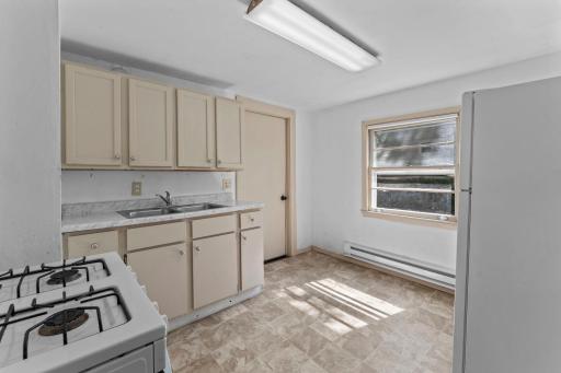 Tiled kitchen with base board heating and entry to the lower level primary bedroom