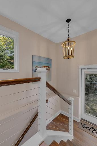 Head downstairs and discover more of what this home has to offer! The staircase features wood handrails and cable railings, with a side door providing convenient access to the outdoor paver patio and firepit area.