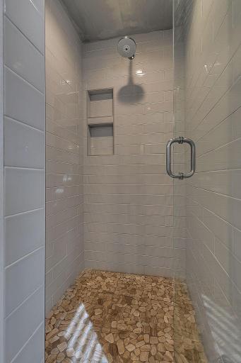 The tiled walk-in shower features a glass enclosure, pebble-style flooring, and recessed niches for convenient storage.