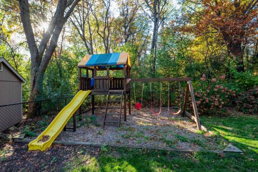 Backyard swing set with a slide and elevated playhouse.